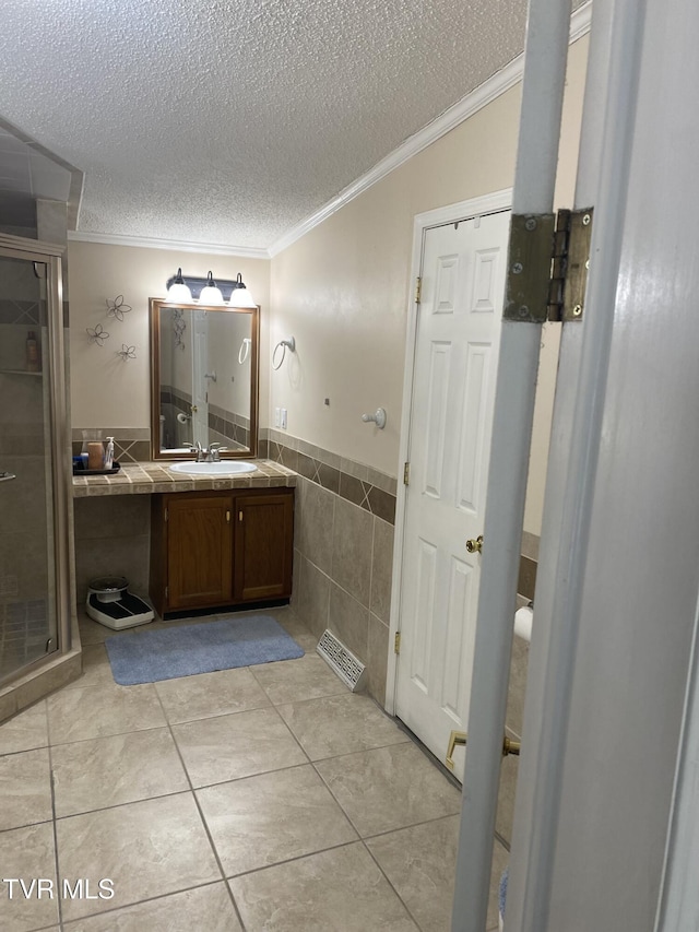 bathroom with visible vents, a stall shower, a textured ceiling, crown molding, and tile walls