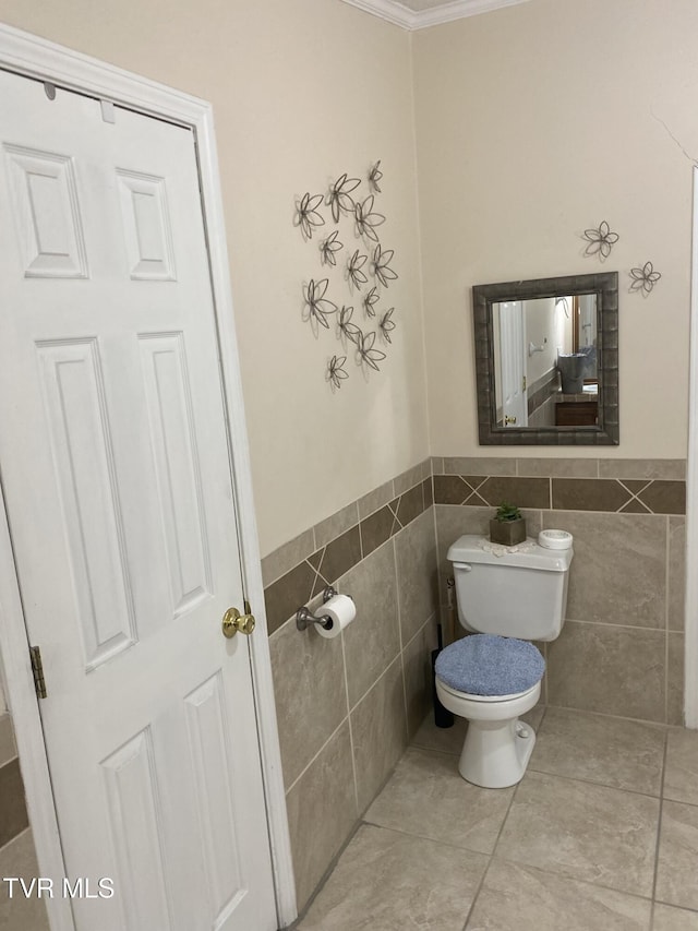 bathroom featuring tile patterned flooring, tile walls, toilet, and wainscoting