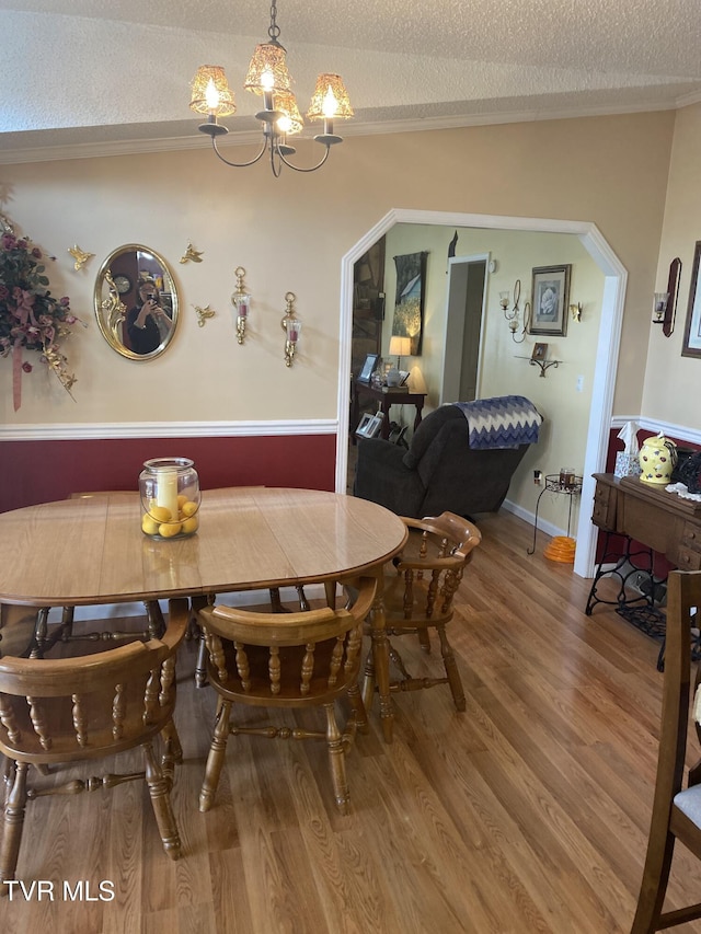 dining space with arched walkways, a textured ceiling, an inviting chandelier, and wood finished floors