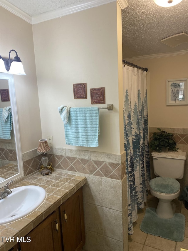 bathroom with a wainscoted wall, tile patterned flooring, a textured ceiling, tile walls, and toilet