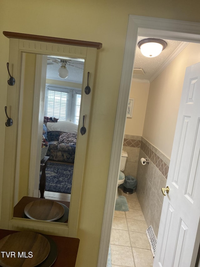 ensuite bathroom with tile patterned floors, toilet, a textured ceiling, tile walls, and crown molding