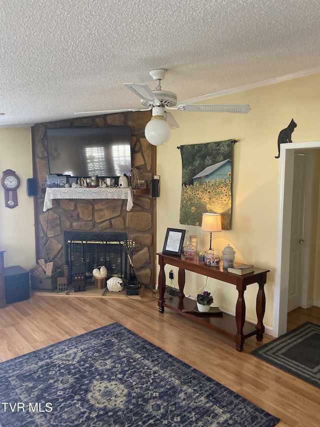 living room with a stone fireplace, a textured ceiling, ceiling fan, and wood finished floors