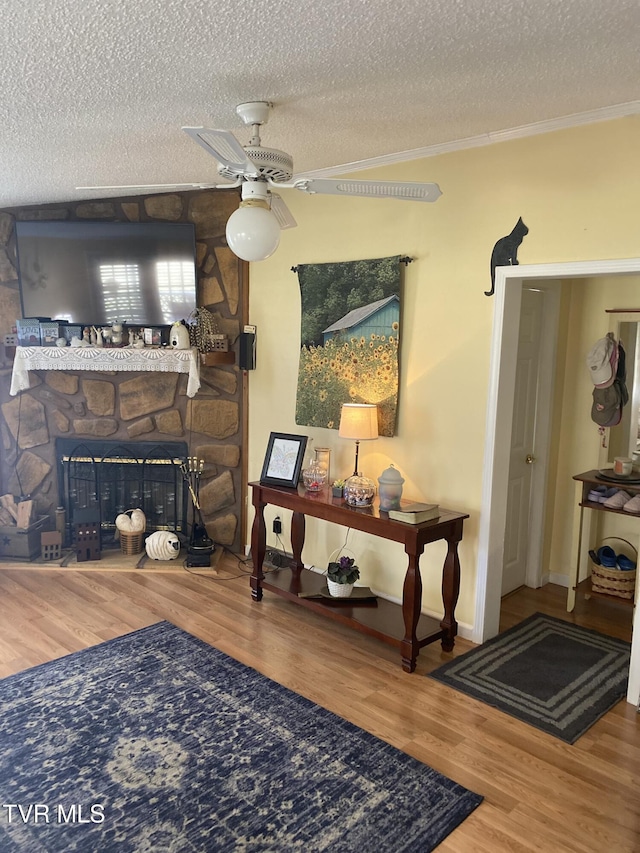 living area with a fireplace, a textured ceiling, crown molding, and wood finished floors