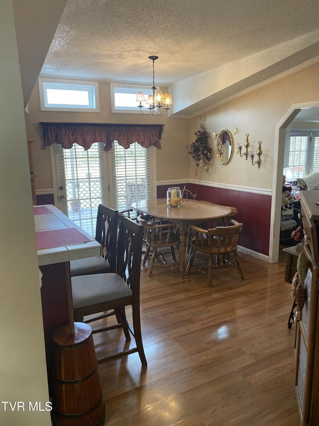 dining room featuring wainscoting, wood finished floors, arched walkways, a notable chandelier, and a textured ceiling