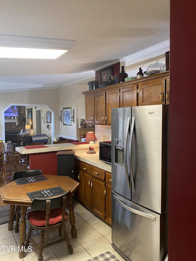 kitchen with ornamental molding, a peninsula, stainless steel fridge with ice dispenser, light countertops, and light tile patterned floors