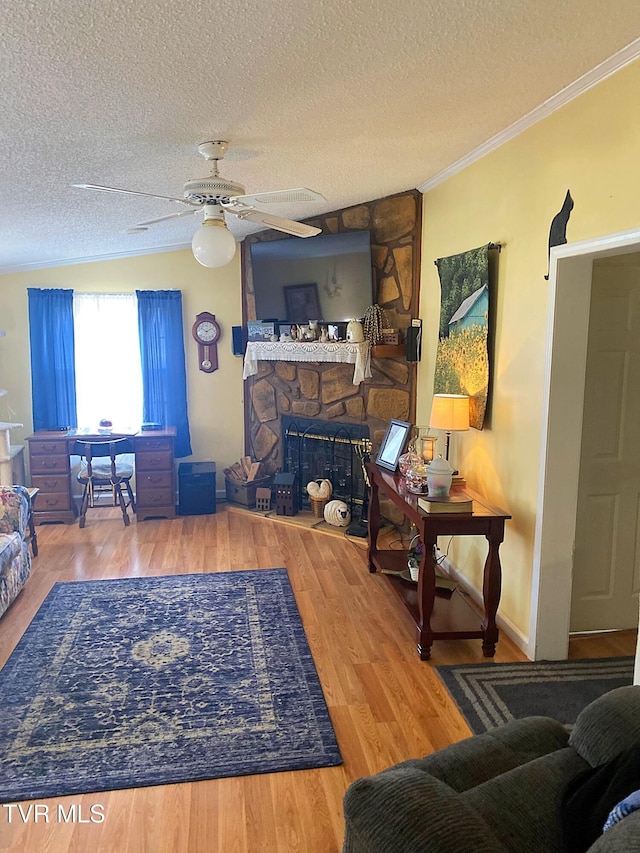 living area featuring a textured ceiling, wood finished floors, a fireplace, and crown molding