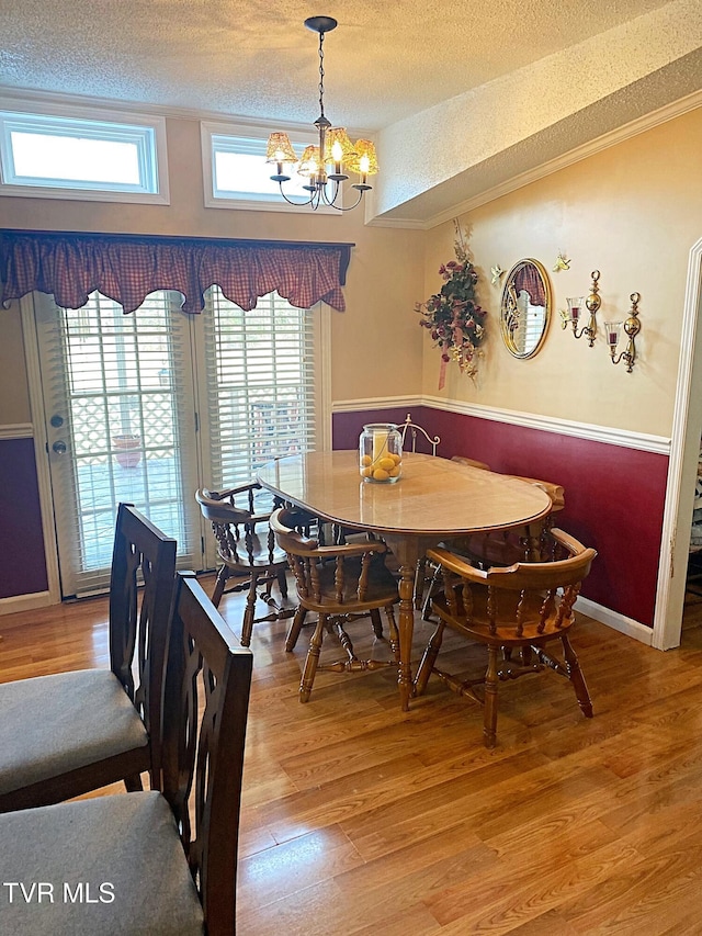 dining room with a textured ceiling, wood finished floors, an inviting chandelier, crown molding, and baseboards