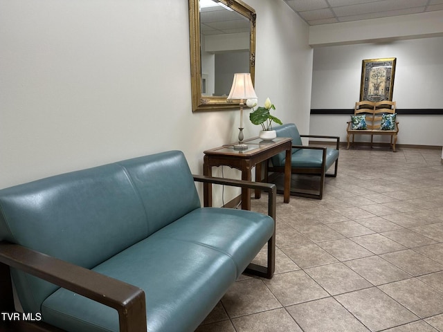 living area featuring light tile patterned floors, a paneled ceiling, and baseboards