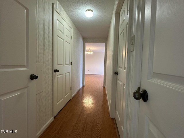 hall featuring baseboards, a textured ceiling, and wood finished floors