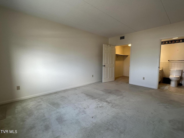 unfurnished bedroom with baseboards, visible vents, a spacious closet, ensuite bathroom, and light carpet