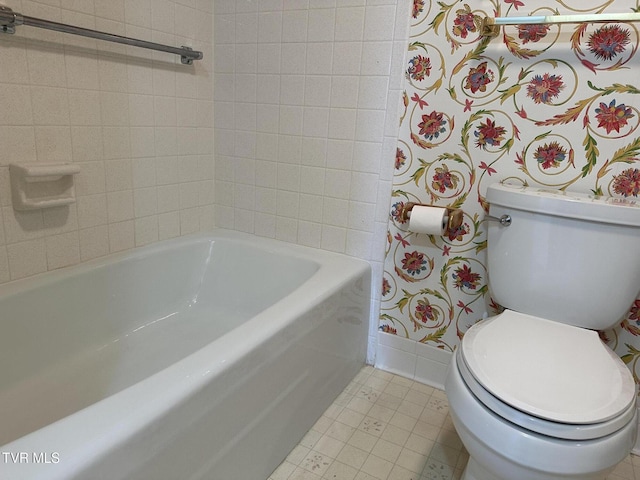 bathroom featuring tile patterned floors, toilet, a tub, wallpapered walls, and baseboards