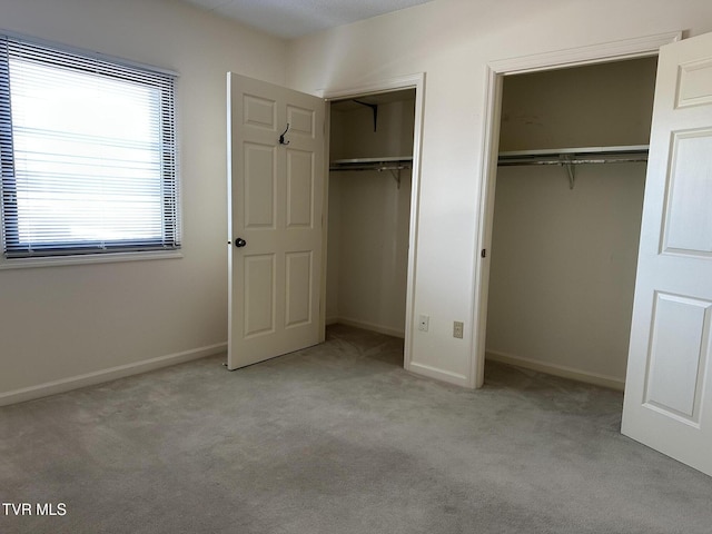 unfurnished bedroom with baseboards, two closets, and carpet floors