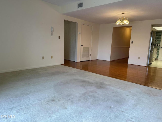 carpeted spare room with visible vents, baseboards, an inviting chandelier, and wood finished floors