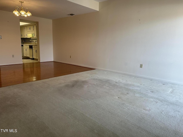 spare room featuring an inviting chandelier, carpet, and baseboards