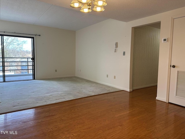 empty room with visible vents, baseboards, an inviting chandelier, wood finished floors, and a textured ceiling