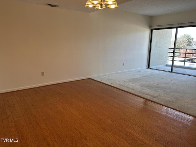 empty room featuring visible vents, wood finished floors, baseboards, and a chandelier