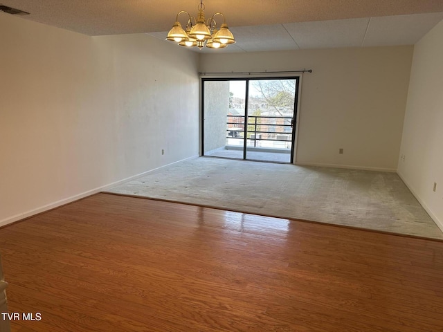 empty room with a chandelier, visible vents, baseboards, and wood finished floors