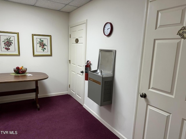 corridor with a drop ceiling, baseboards, and dark carpet