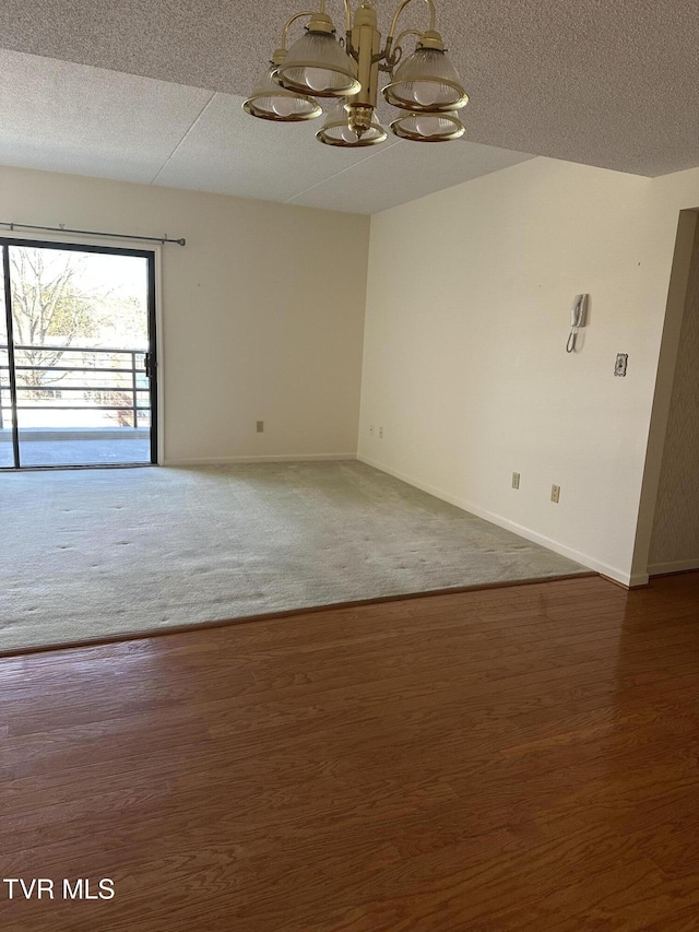 empty room featuring a notable chandelier, wood finished floors, baseboards, and a textured ceiling