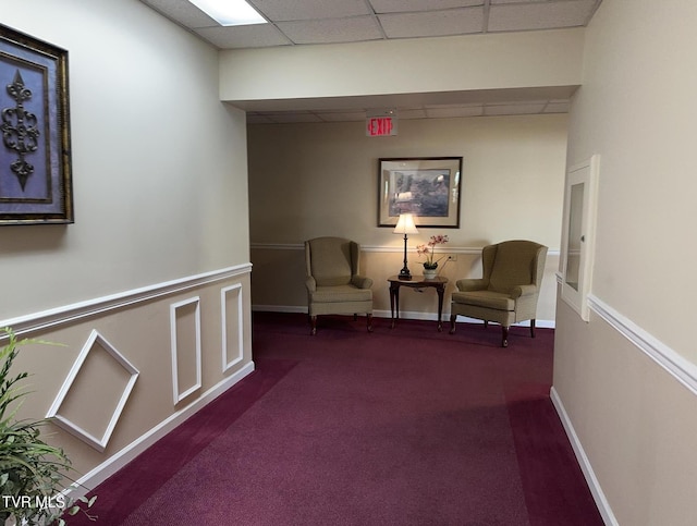 living area featuring dark colored carpet, baseboards, and a paneled ceiling