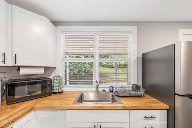 kitchen featuring freestanding refrigerator, a sink, decorative backsplash, white cabinets, and butcher block counters