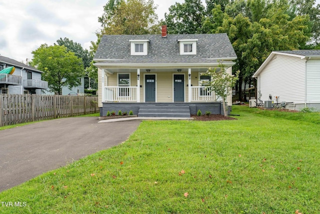 bungalow with a front lawn, a porch, fence, roof with shingles, and central AC unit