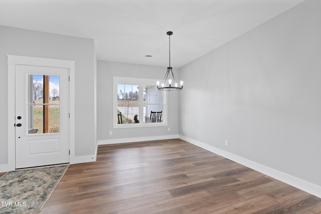 unfurnished dining area with baseboards, wood finished floors, and a chandelier