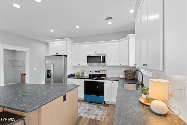 kitchen featuring wood finished floors, visible vents, a sink, appliances with stainless steel finishes, and dark countertops