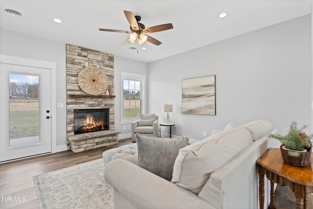 living room with a stone fireplace, recessed lighting, wood finished floors, and visible vents