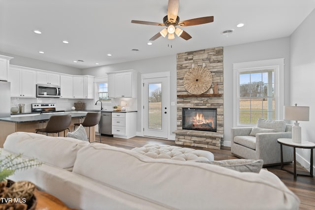 living area featuring wood finished floors, visible vents, a ceiling fan, recessed lighting, and a stone fireplace