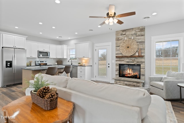 living room featuring dark wood-style floors, visible vents, recessed lighting, and a stone fireplace