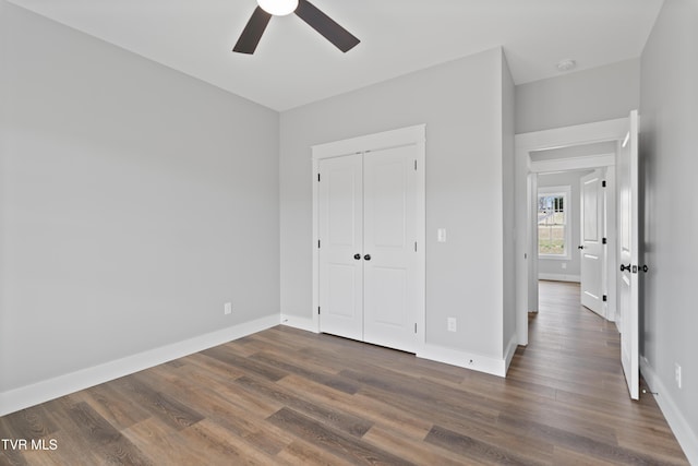 unfurnished bedroom featuring a closet, ceiling fan, baseboards, and dark wood-style flooring