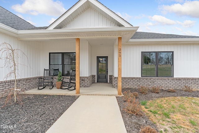 property entrance with brick siding, a porch, and roof with shingles