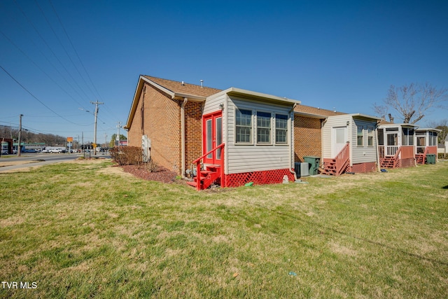 view of home's exterior featuring brick siding, cooling unit, entry steps, and a lawn