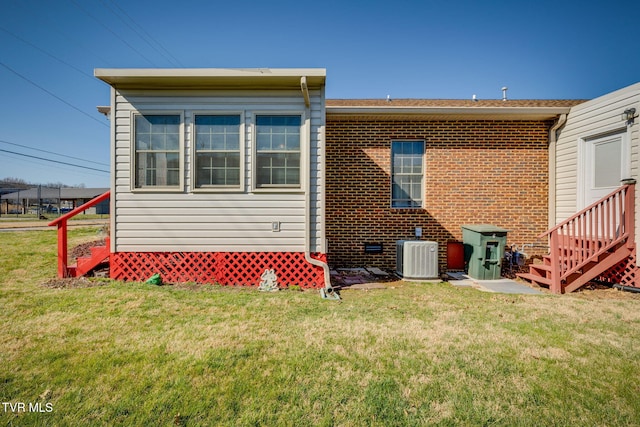 back of property featuring brick siding, a lawn, entry steps, and central AC