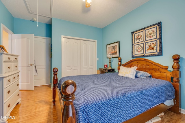 bedroom featuring attic access, a closet, light wood finished floors, and ceiling fan