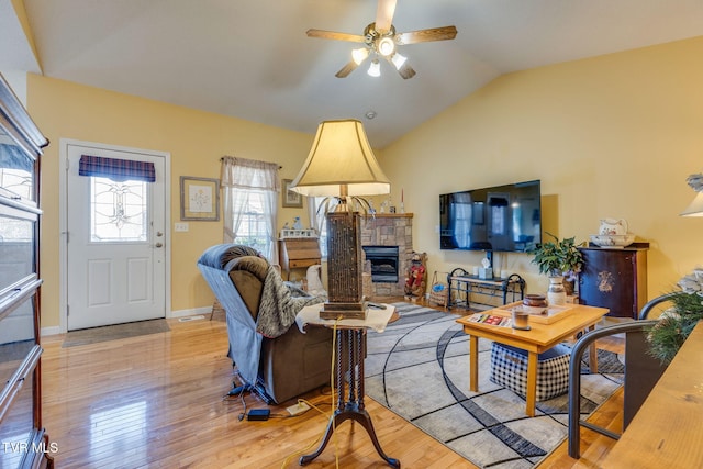 living room with baseboards, ceiling fan, light wood-type flooring, vaulted ceiling, and a fireplace