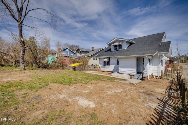 rear view of house featuring entry steps, fence, and roof with shingles