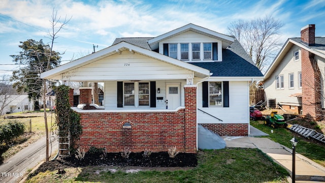 bungalow-style house with brick siding, a shingled roof, fence, covered porch, and central AC unit