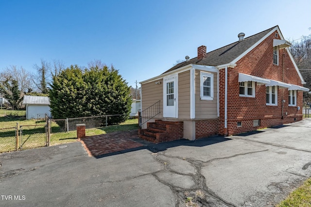 back of house with brick siding, fence, entry steps, a chimney, and a gate