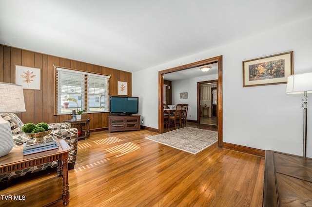 living room featuring baseboards, light wood-style flooring, and wood walls