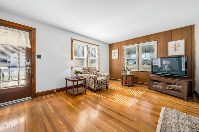 living area with visible vents, baseboards, light wood-style flooring, and wood walls