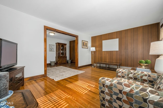 living room featuring baseboards, wooden walls, and wood finished floors