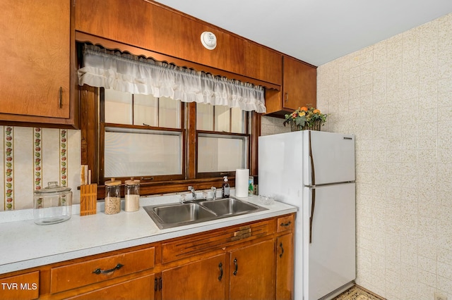 kitchen with a sink, brown cabinetry, light countertops, and freestanding refrigerator