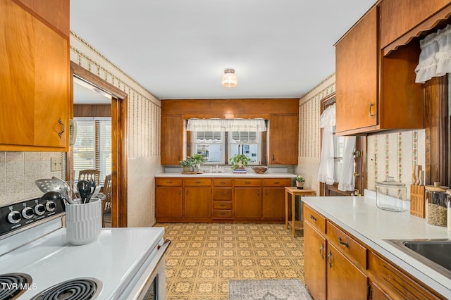 kitchen featuring light countertops, brown cabinetry, light floors, and white range with electric stovetop