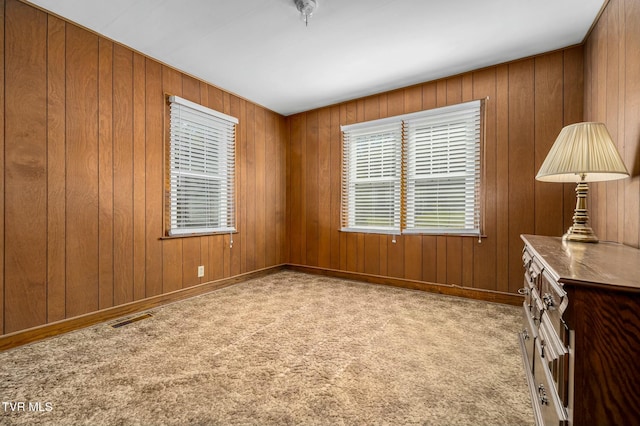 unfurnished room with visible vents, carpet floors, and wooden walls