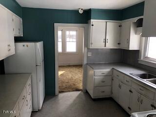 kitchen with a sink, freestanding refrigerator, light countertops, and white cabinetry