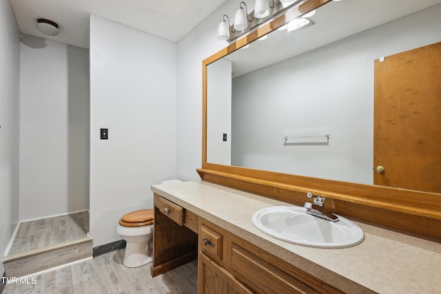 bathroom featuring baseboards, toilet, wood finished floors, and vanity