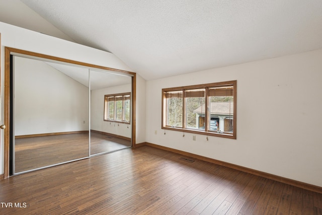 unfurnished bedroom with baseboards, lofted ceiling, hardwood / wood-style flooring, a closet, and a textured ceiling