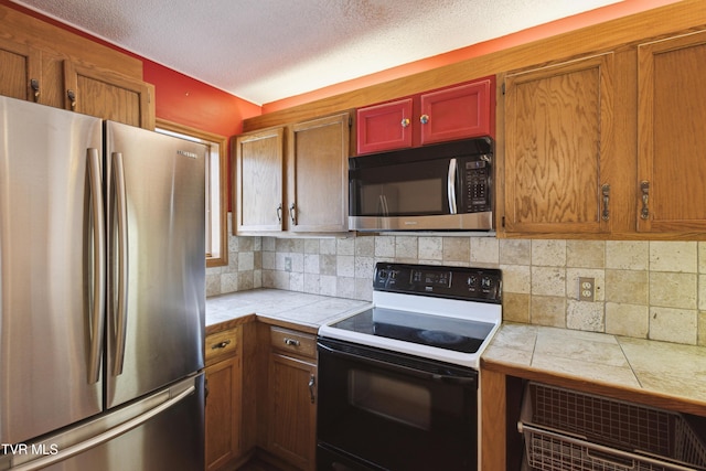 kitchen with range with electric cooktop, backsplash, a textured ceiling, freestanding refrigerator, and tile counters